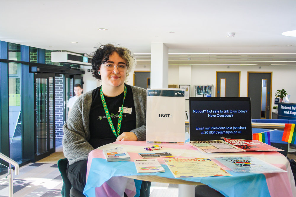 A Marjon student at a table with an LGBTQ society sign