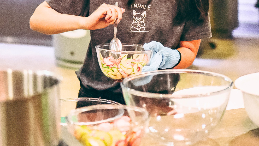 A neck-down shot of a woman cooking in a kitchen. There are mixing bowls on the counter in front of her.