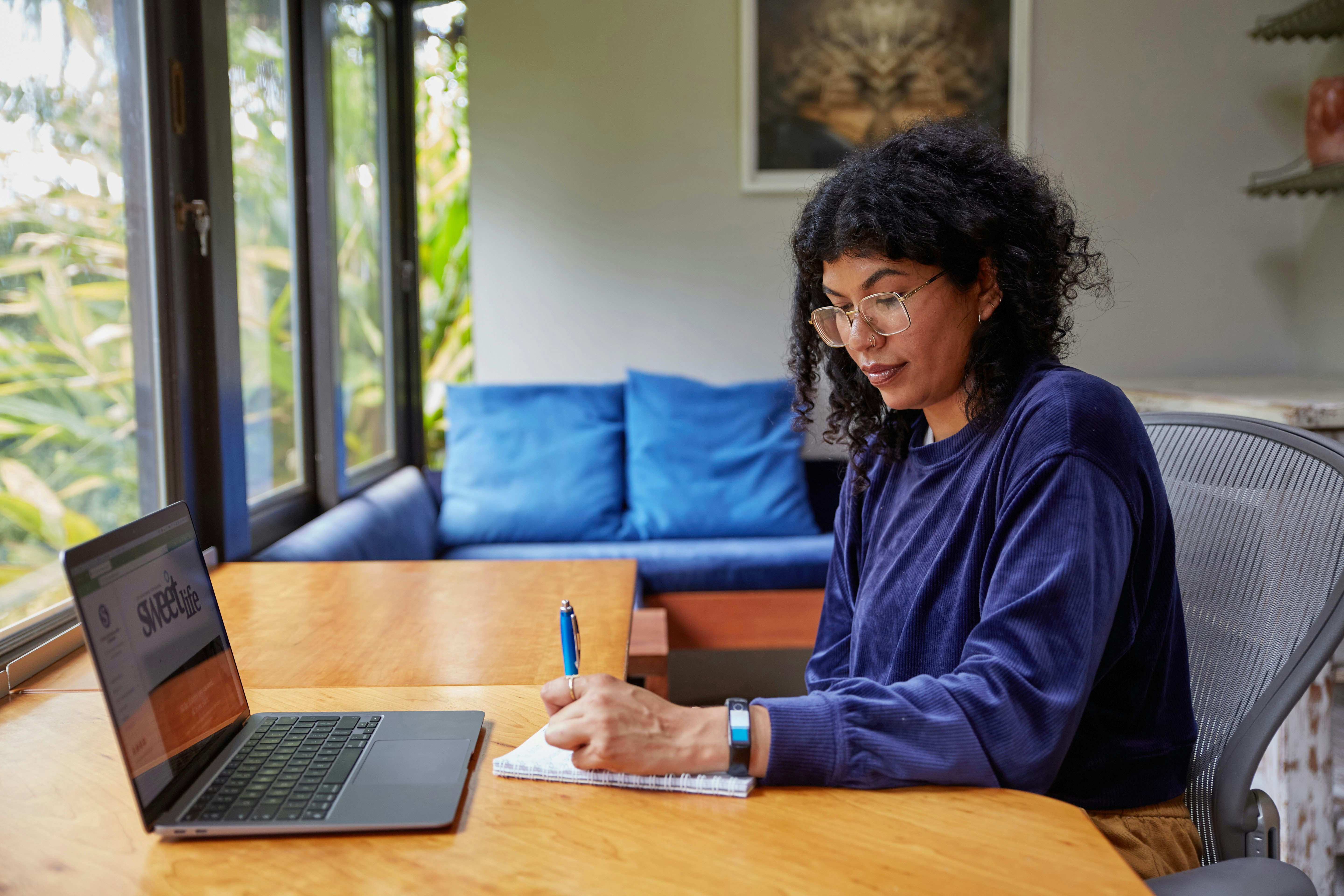 A woman sitting at a table, writing on a notepad and looking at a computer