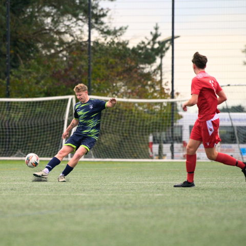 Two male students playing football on an artificial grass pitch.