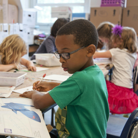 A young boy in a green t-shirt sitting at a desk working