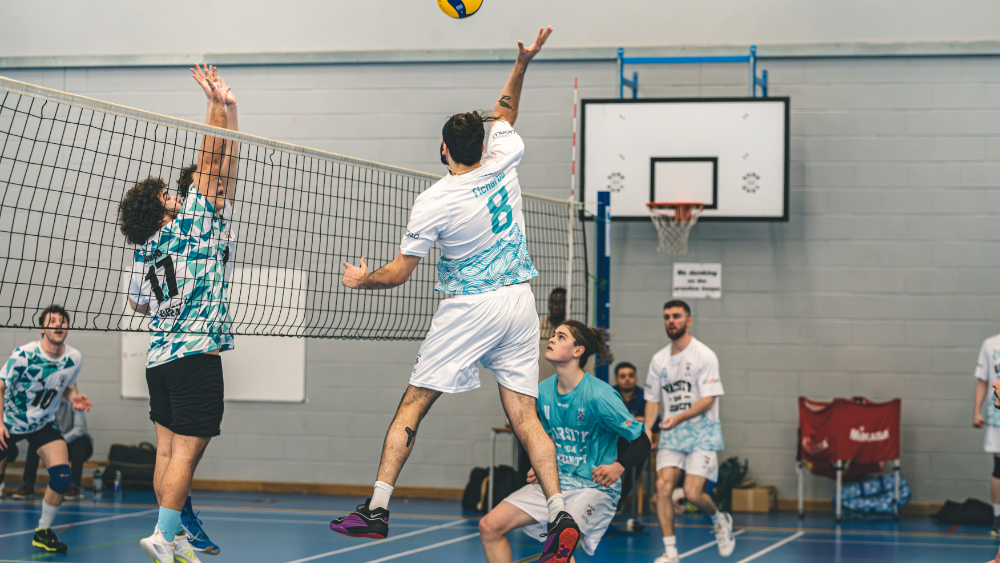 Marjon men's volleyball team playing a match. One of them has just smacked the ball over the net.