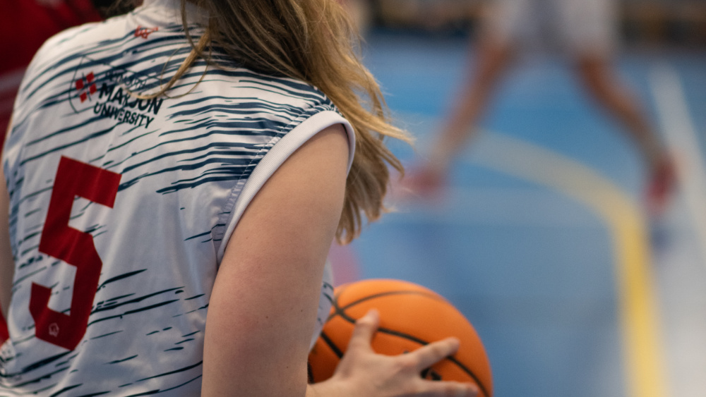 An over-shoulder torso shot of a woman holding a basketball